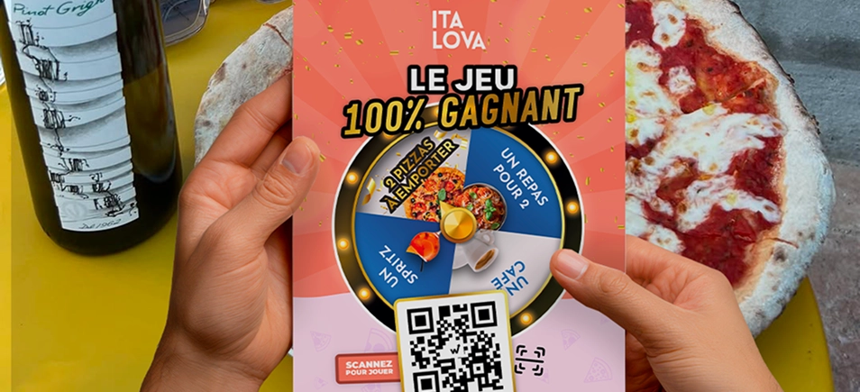 Flyer du jeu 100% gagnant Italova avec roue à cadeaux et QR code, tenu au-dessus d'une table avec pizza