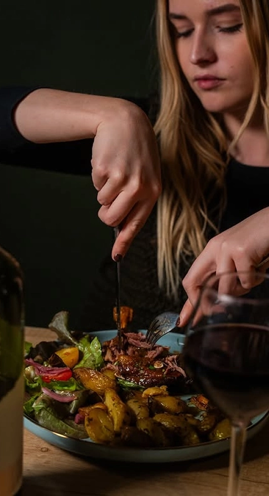 Cliente coupant une pièce de viande accompagnée d'un verre de vin rouge à l'Izard Café Central