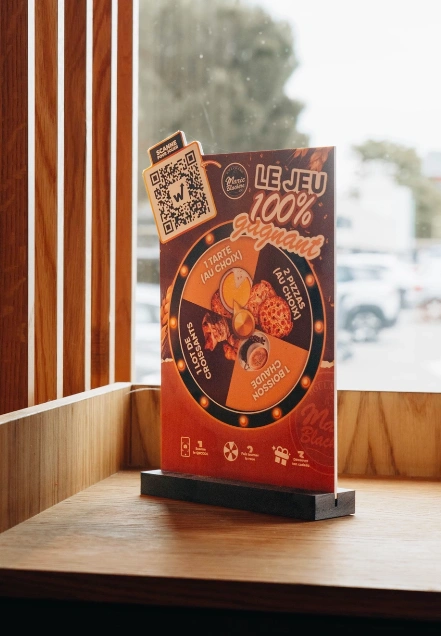 Chevalet du jeu 100% gagnant Marie Blachère avec QR code posé près de la vitre de la boulangerie