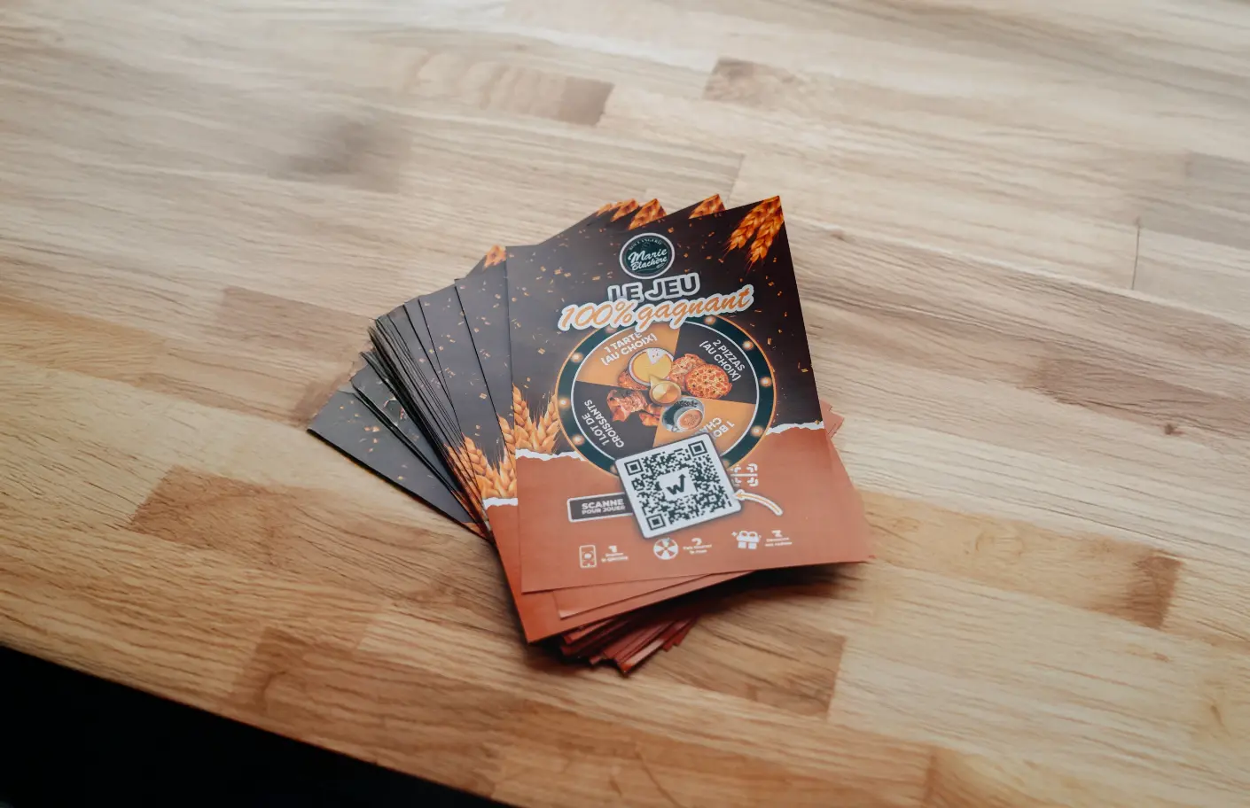 Flyers du jeu 100% gagnant Marie Blachère avec roue à cadeaux et QR code étalés sur une table en bois