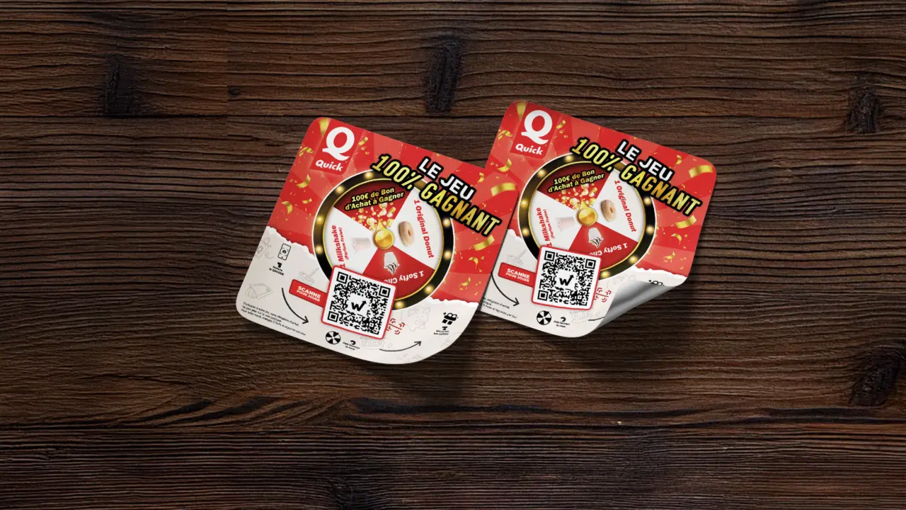 Stickers du jeu concours Quick avec QR code et lots à gagner posés sur une table en bois