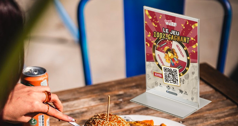 Chevalet du jeu concours Rouge Beef avec QR code posé sur une table en terrasse à côté d'un burger