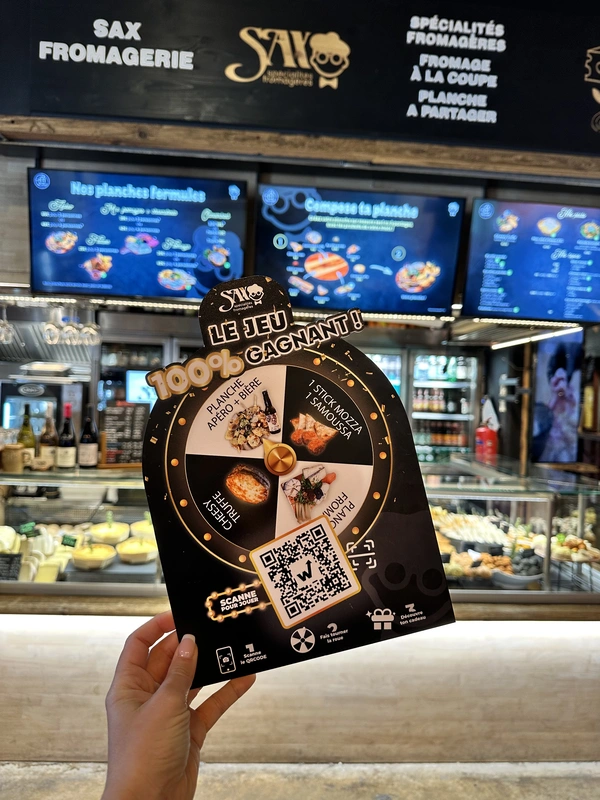 PLV du jeu concours Sax « Le jeu 100 % gagnant » avec roue à cadeaux et QR code devant le comptoir de la fromagerie