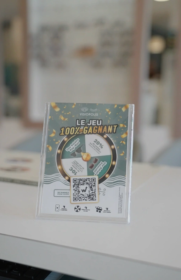 Chevalet du jeu concours Visiopolis « Le jeu 100 % gagnant » avec roue à cadeaux et QR code sur le comptoir du magasin d'optique